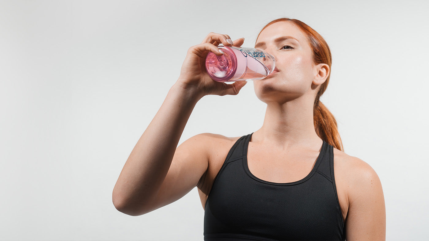 Junge Frau trinkt ein Glas Wasser mit Hydration Helper